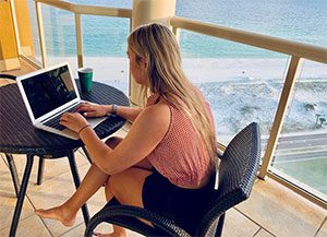 woman working-on-writing-a-blog-on-a-laptop-barefoot-on-a-balcony-at-the-beach